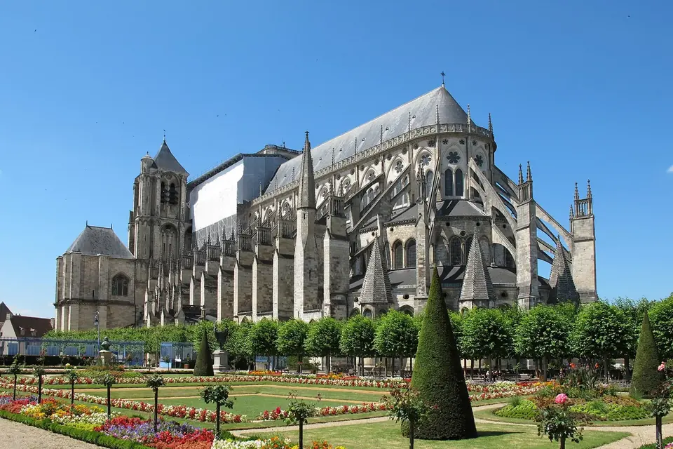 La cathédrale gothique Saint-Étienne de Bourges vue depuis un jardin à la française fleuri, sous un ciel bleu