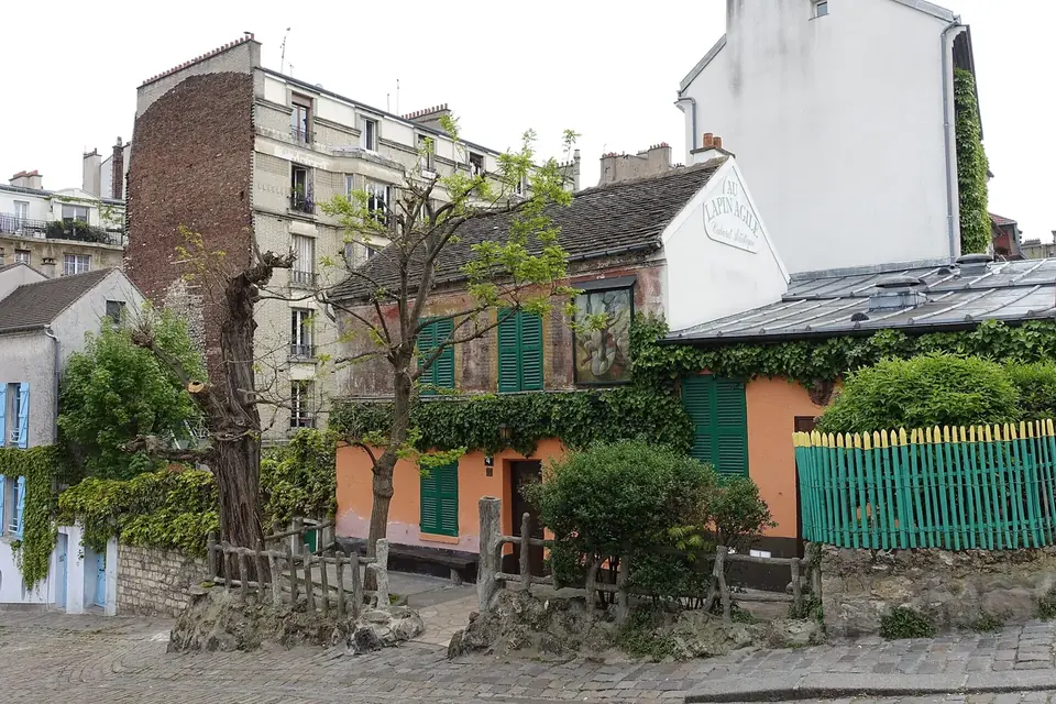 Une petite maison rose aux volets verts entourée d'arbres, sur une rue pavée en pente de Montmartre