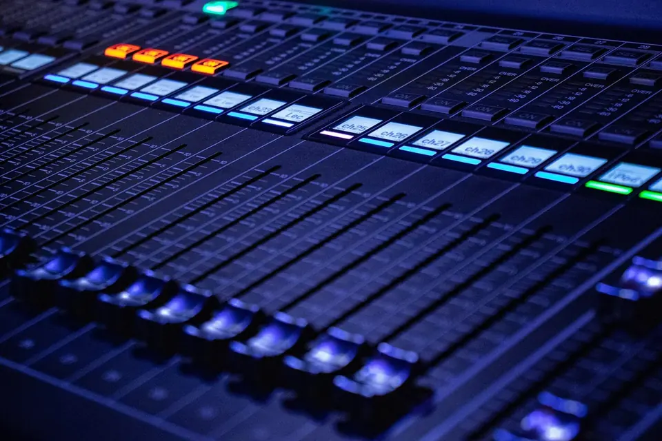 Gros plan sur les curseurs et les boutons lumineux bleus et orange d'une console de mixage de studio
